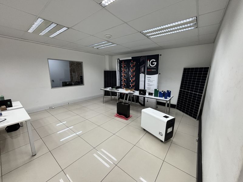 A clean, functional office space featuring tiled flooring, a suspended ceiling with recessed lighting, and an internal window looking into an adjacent area.