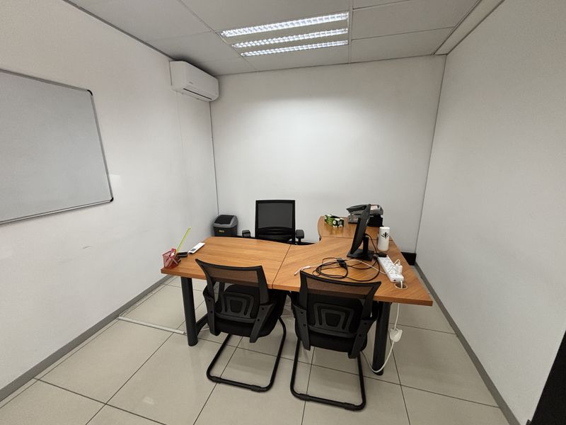 A functional office space featuring tiled flooring, recessed ceiling lighting, and a wall-mounted air conditioning unit.
