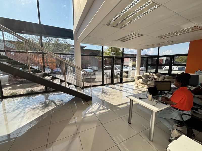 Modern industrial office entry featuring floor-to-ceiling glass windows, tiled flooring, and a contemporary steel staircase with cable railing.