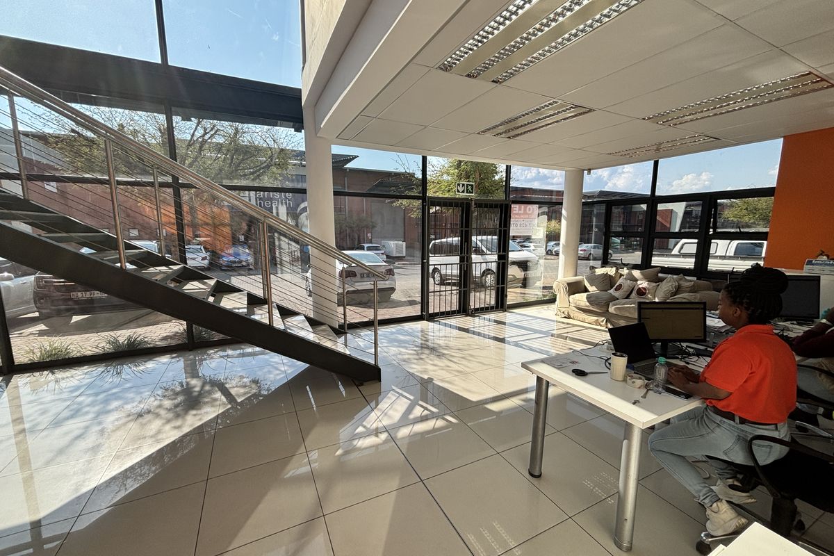Modern industrial office entry featuring floor-to-ceiling glass windows, tiled flooring, and a contemporary steel staircase with cable railing.