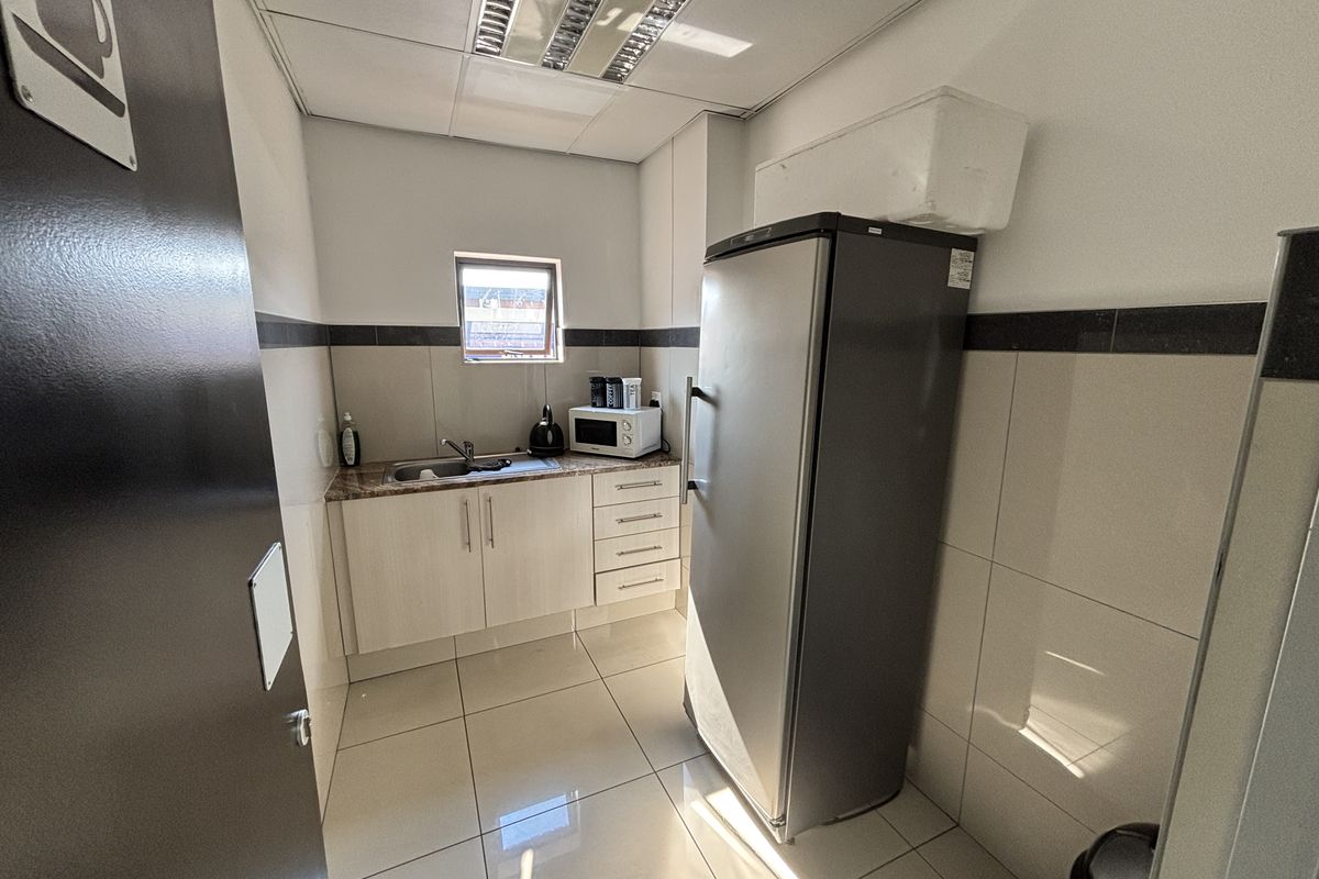A compact industrial kitchenette featuring tiled walls and flooring, built-in cabinetry with a stainless steel sink, and recessed ceiling lighting.