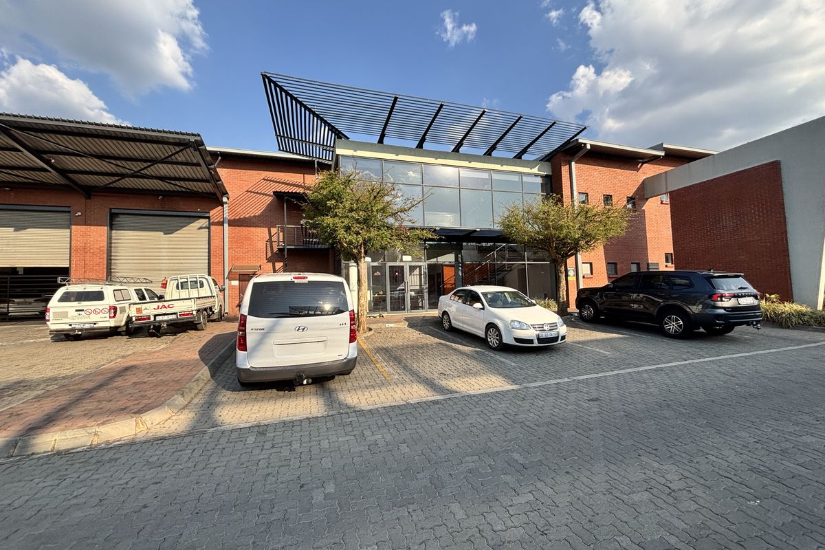 Front elevation of an industrial property featuring a brick facade, large glass entrance, metal canopy, and a paved parking area with roller shutter access.