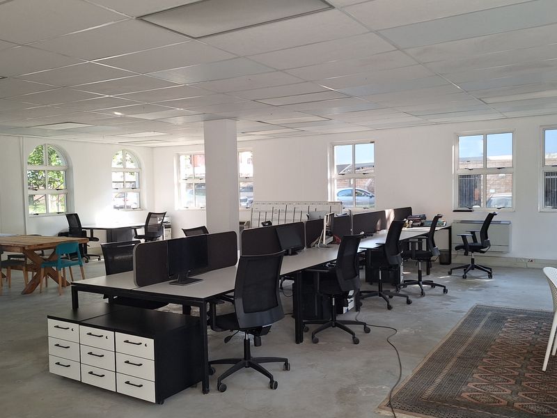 Spacious open-plan office area featuring a suspended ceiling, large arched windows, and polished concrete flooring, providing a functional workspace environment.