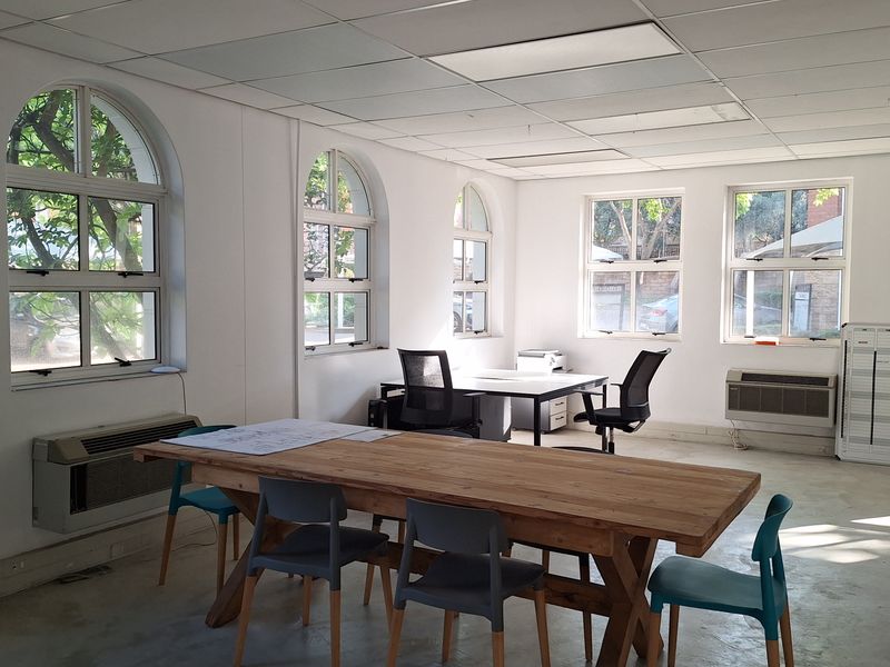 A spacious office area featuring arched windows, suspended ceiling tiles, and concrete flooring, equipped with wall-mounted HVAC units for climate control.