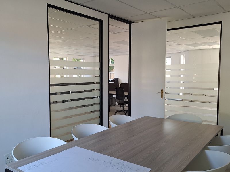 A professional office meeting room featuring modern frosted glass partitions and a suspended ceiling, providing a bright and functional workspace environment.