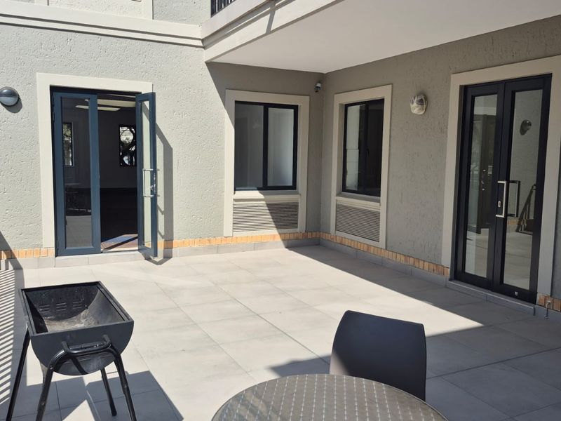 A spacious, well-maintained outdoor patio area featuring tiled flooring, modern double glass doors, and external wall lighting, suitable for office break-out space.