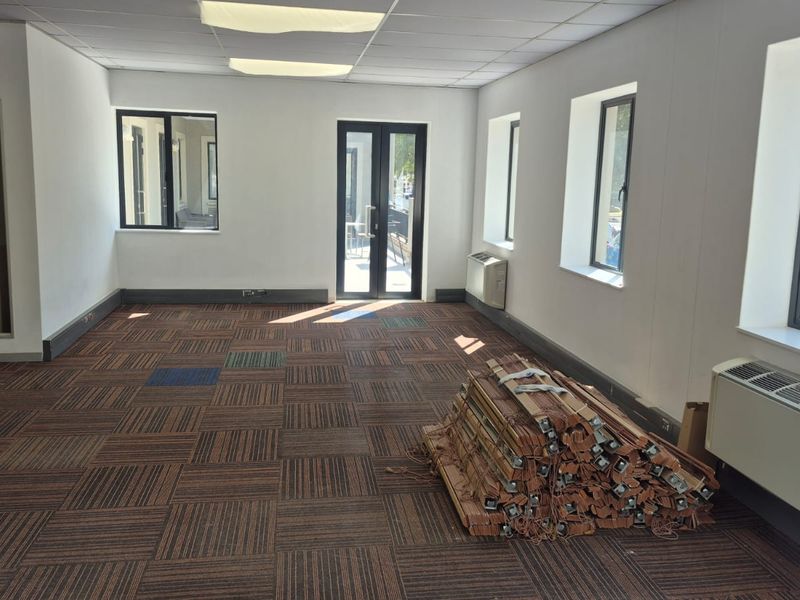 A spacious, vacant office area featuring carpet tiles, suspended ceilings, multiple windows, and integrated HVAC units, offering a clean and functional workspace.