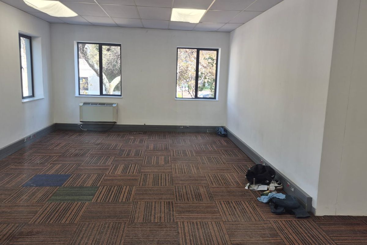 A vacant office space featuring suspended ceilings, recessed lighting, and carpet tile flooring, equipped with a wall-mounted air conditioning unit.