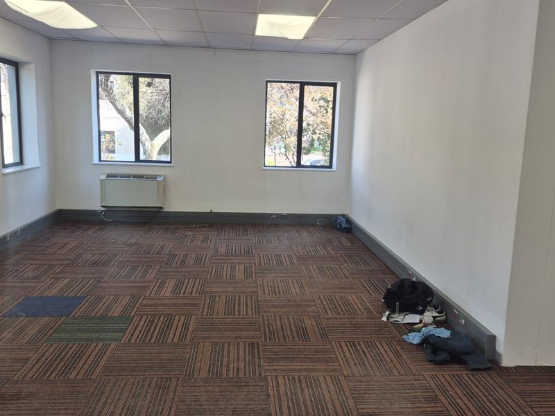 A vacant office space featuring suspended ceilings, recessed lighting, and carpet tile flooring, equipped with a wall-mounted air conditioning unit.