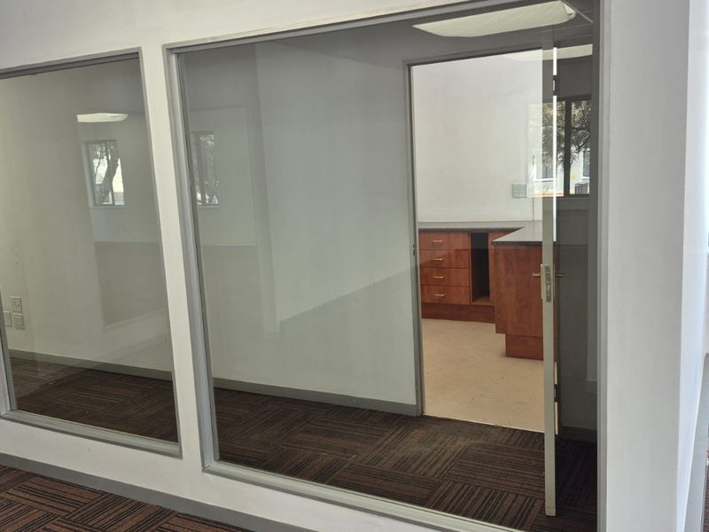 A bright office space featuring glass partitions, carpet tiles, and built-in cabinetry, offering a clean and professional environment suitable for various business needs.