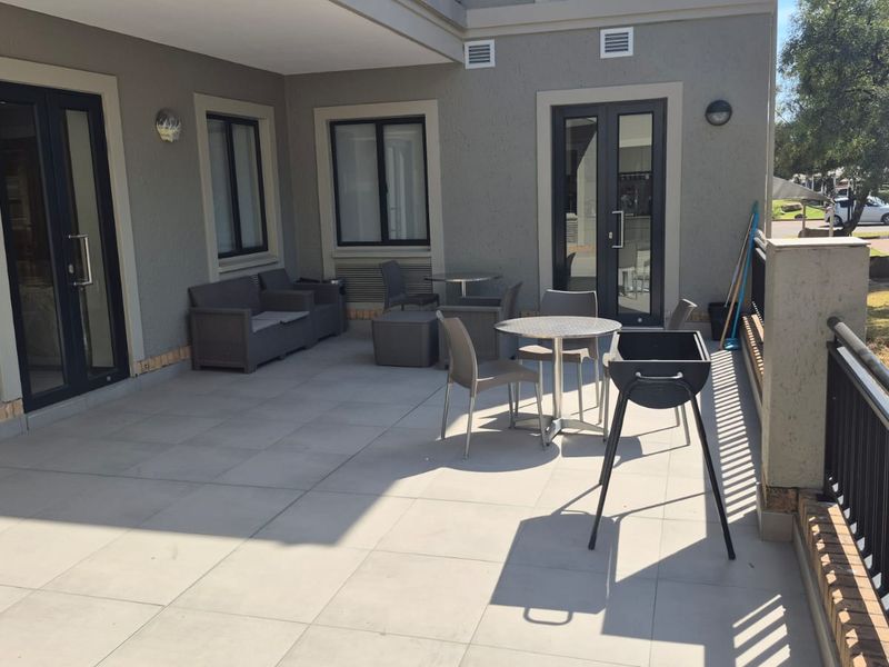 A spacious covered patio area featuring tiled flooring, modern double glass doors, and a metal safety railing, providing a functional outdoor space.