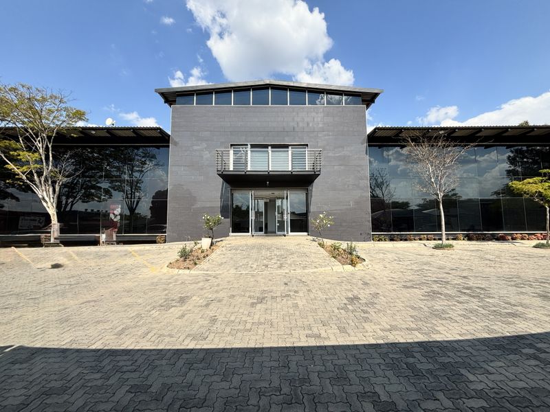 Modern industrial office building featuring a prominent stone-clad facade, extensive glass curtain walls, and a paved entrance area.