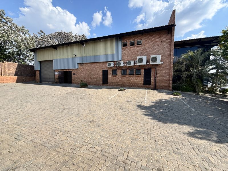 Industrial property exterior featuring a brick and metal facade, roller shutter door, and dedicated paved parking area with multiple external air conditioning units.