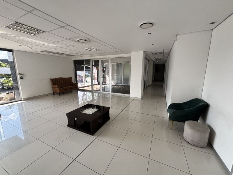 Spacious industrial entrance lobby featuring tiled flooring, suspended ceilings with recessed lighting, and large glass doors providing ample natural light.