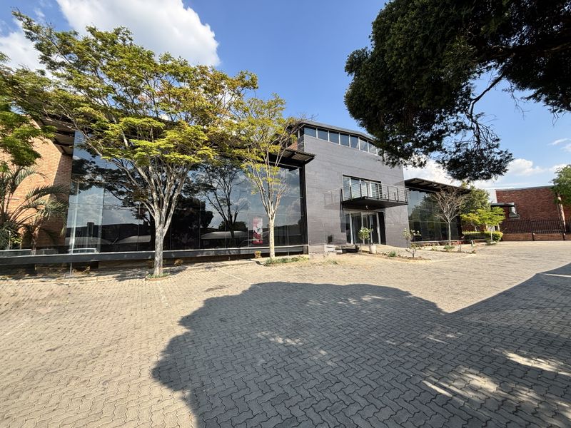 Modern industrial building featuring a large glass curtain wall, brick facade, and a paved driveway entrance with a small balcony.
