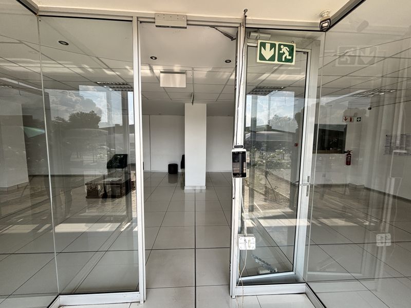 A bright, open-plan industrial entrance area featuring glass doors, tiled flooring, and a suspended ceiling with integrated lighting and security access systems.