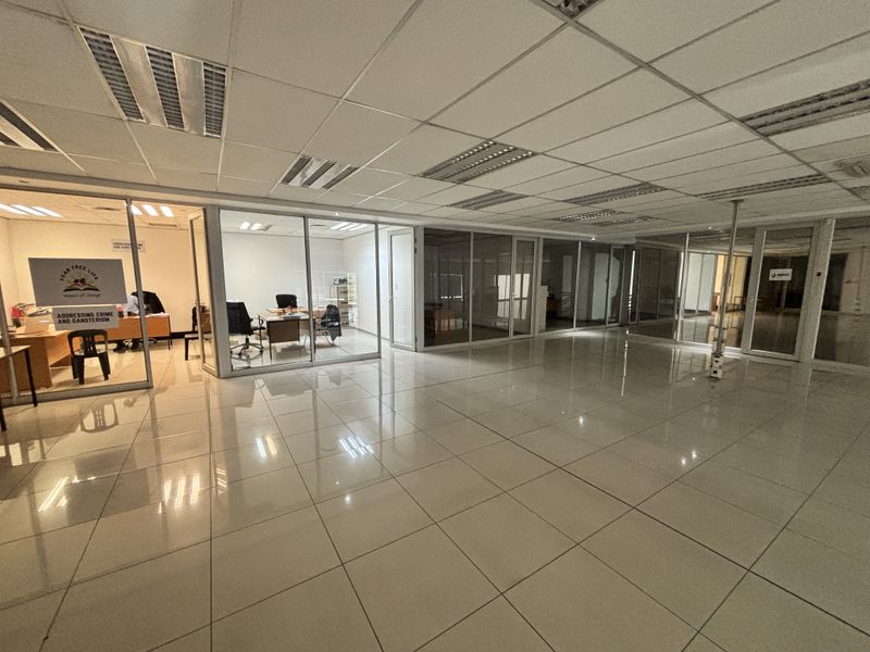 Spacious industrial office area featuring glass-partitioned private offices, suspended ceilings with recessed lighting, and polished tiled flooring throughout.