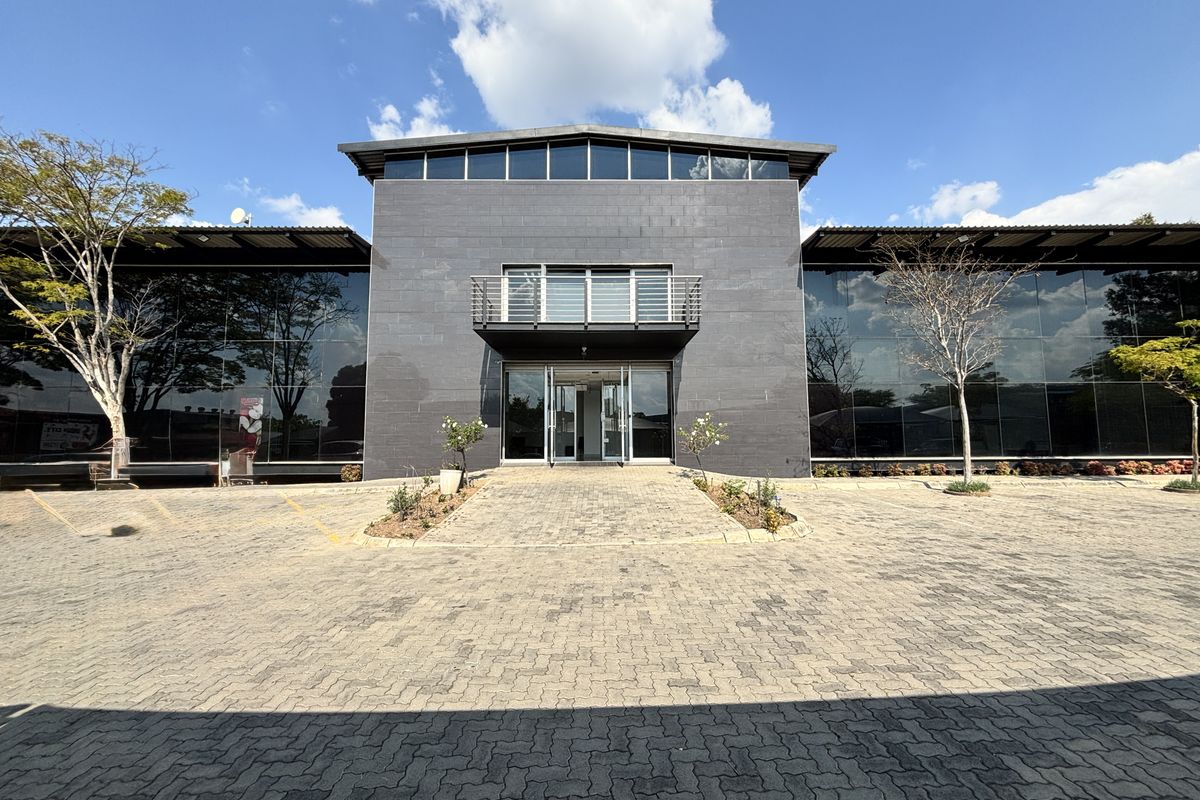 Modern industrial office building featuring a prominent stone-clad facade, extensive glass curtain walls, and a paved entrance area.