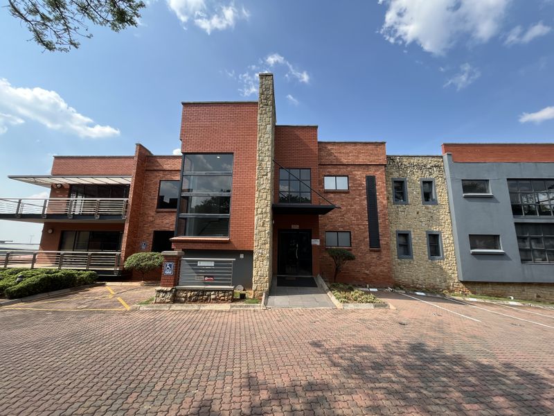 Front elevation of a modern office building featuring a mix of red brick and stone cladding, with a paved driveway and balcony access.