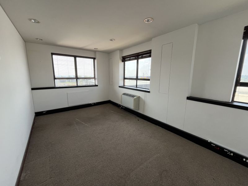 A vacant office space featuring neutral walls, carpeted flooring, recessed lighting, and an integrated HVAC unit with large windows providing natural light.