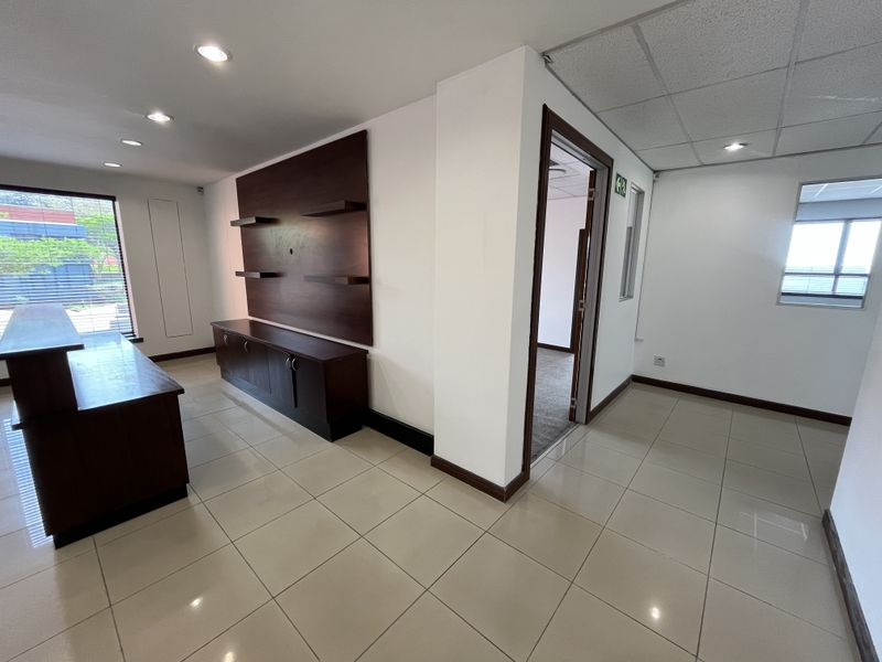 A bright, open-plan office space featuring tiled flooring, recessed lighting, and built-in cabinetry, offering a clean and professional environment.