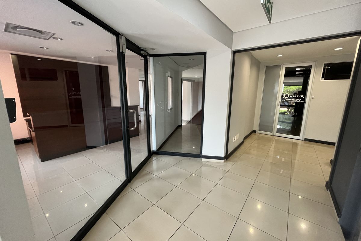 Modern office interior featuring glass partition walls, tiled flooring, and recessed downlighting, creating a professional and open workspace environment.