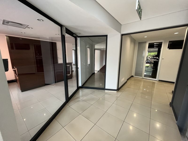 Modern office interior featuring glass partition walls, tiled flooring, and recessed downlighting, creating a professional and open workspace environment.