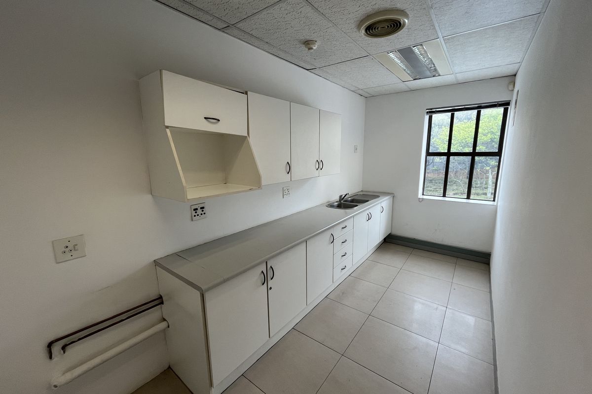 A functional office kitchenette featuring built-in white cabinetry, a stainless steel sink, tiled flooring, and a drop ceiling with integrated lighting.