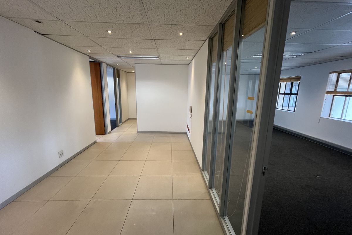 Empty office space featuring a mix of tiled and carpeted flooring, glass partition walls, and a suspended ceiling with recessed lighting.