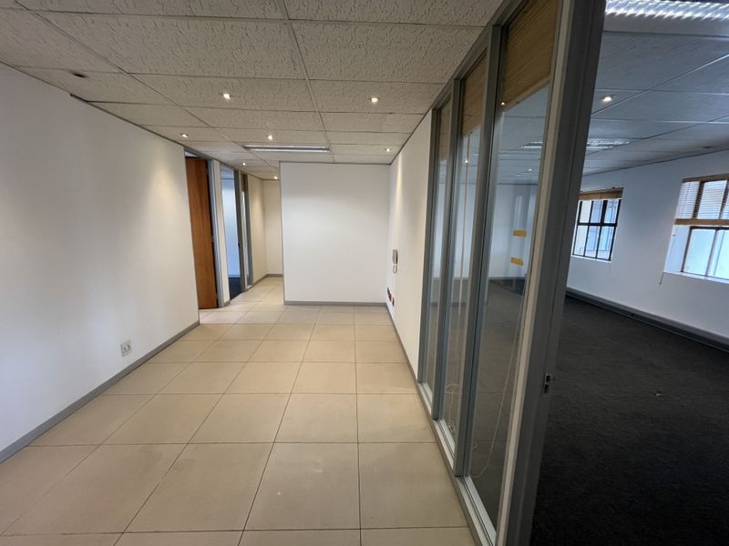 Empty office space featuring a mix of tiled and carpeted flooring, glass partition walls, and a suspended ceiling with recessed lighting.