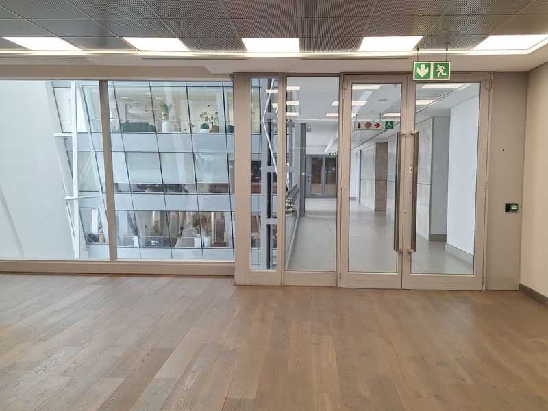 Modern, open-plan office space featuring high-quality timber flooring, recessed LED lighting, and extensive glass partitioning providing natural light and a professional aesthetic.