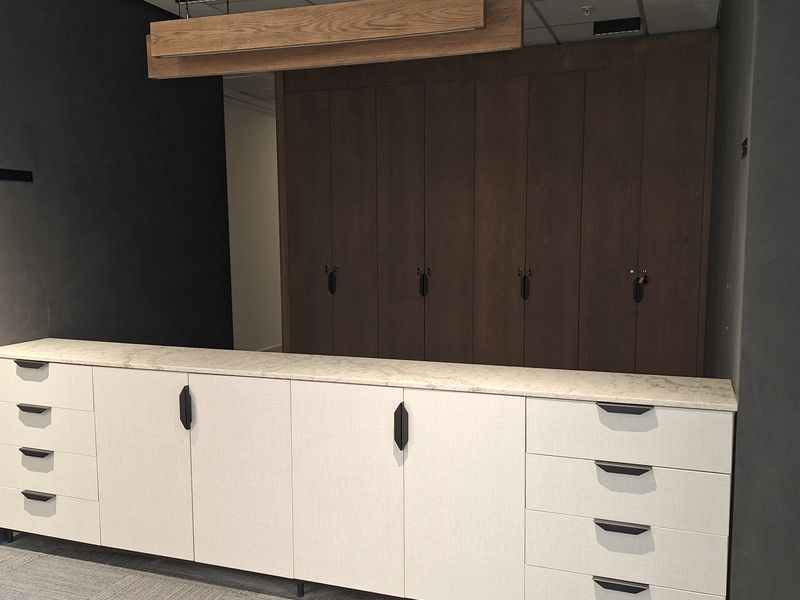 A modern office storage area featuring custom built-in cabinetry with stone countertops, integrated timber lighting, and professional carpet tile flooring.