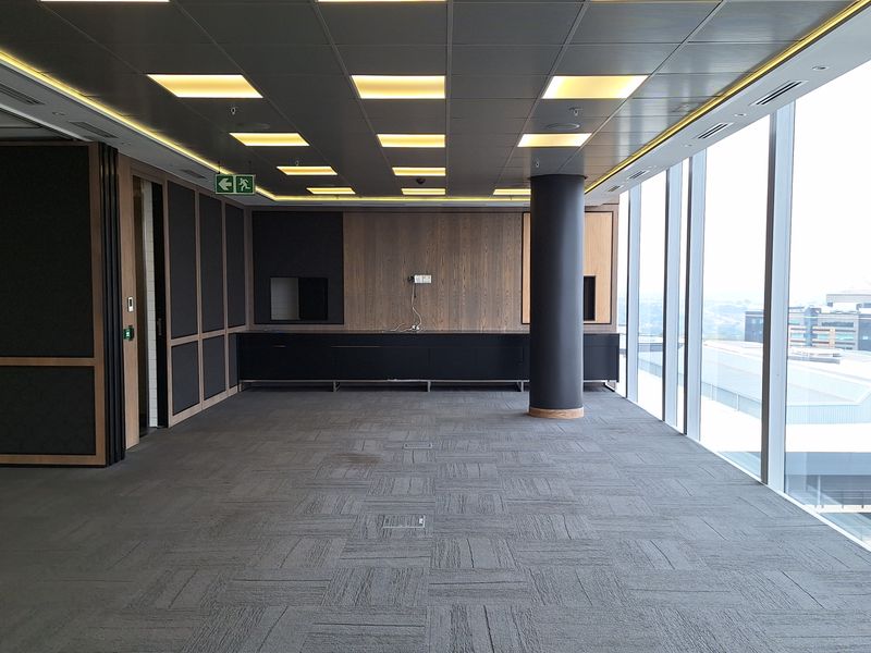 A modern, vacant office space featuring floor-to-ceiling windows, recessed ceiling lighting, built-in cabinetry, and carpeted flooring with integrated floor power boxes.