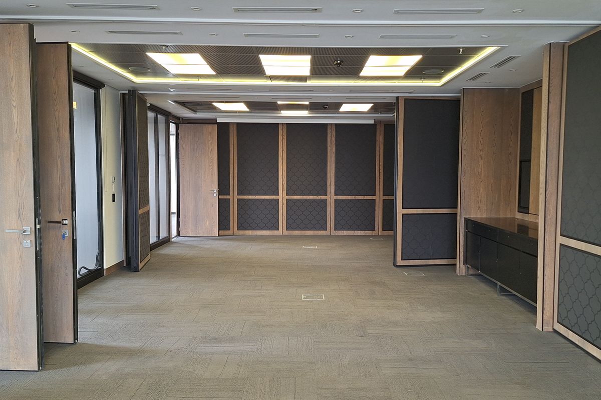 Spacious, empty office area featuring modern wood paneling, recessed ceiling lighting, carpeted flooring, and integrated floor power outlets.
