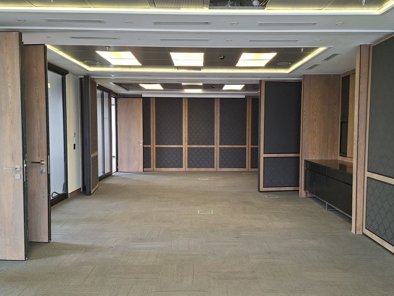 Spacious, empty office area featuring modern wood paneling, recessed ceiling lighting, carpeted flooring, and integrated floor power outlets.