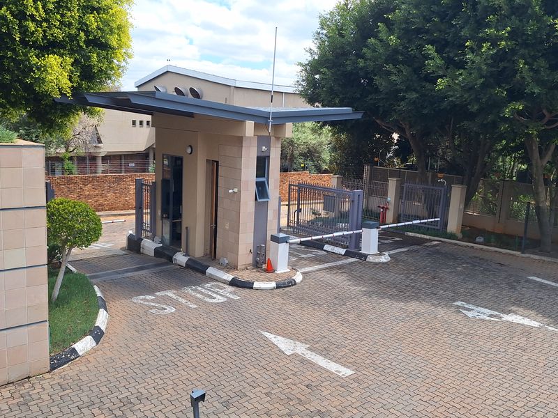 A secure office park entrance featuring a guard house, automated boom gate, and paved driveway with clear traffic markings.