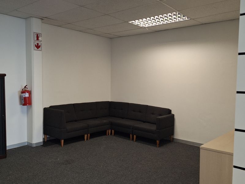 A functional office space featuring a suspended ceiling with recessed lighting, grey carpeting, and a wall-mounted fire extinguisher.