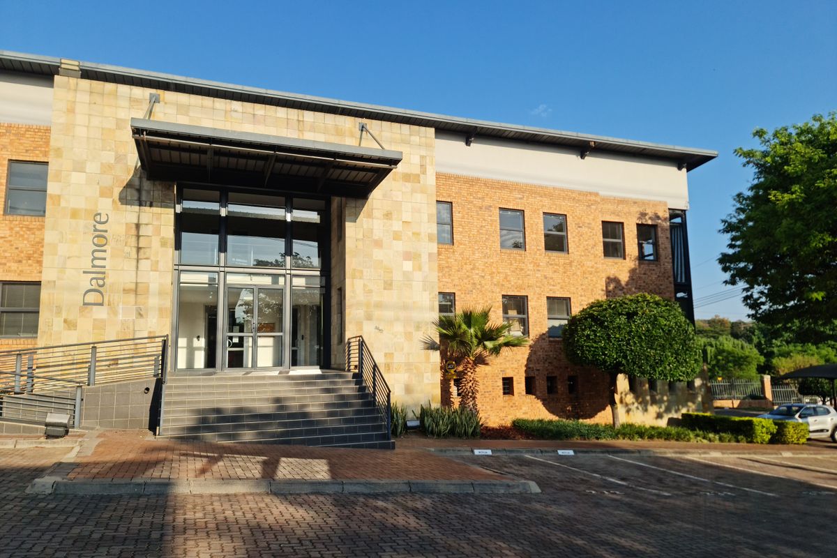 Front elevation of the Dalmore office building featuring a stone and brick facade, glass entrance, and paved parking area.