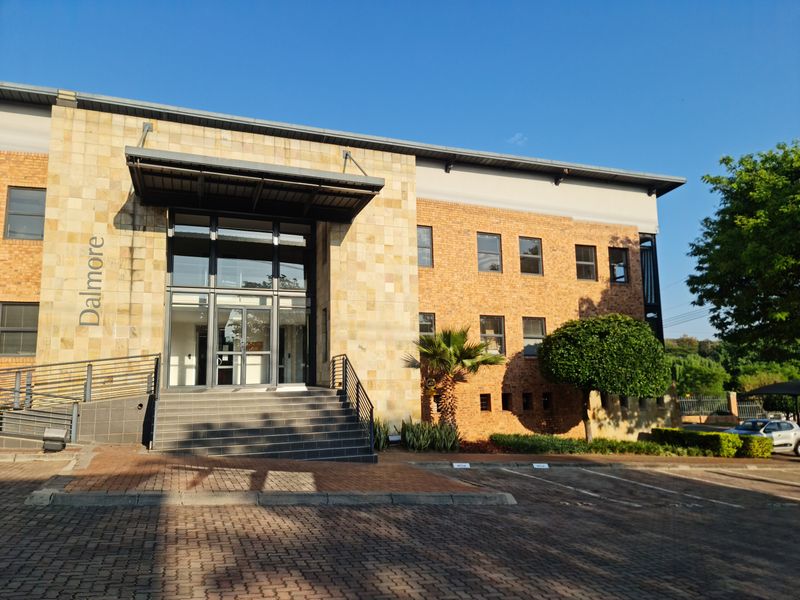 Front elevation of the Dalmore office building featuring a stone and brick facade, glass entrance, and paved parking area.