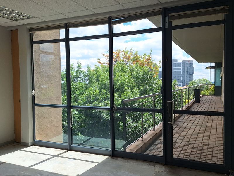 Empty office space featuring a suspended ceiling, recessed lighting, and large glass doors opening onto a private balcony with urban views.
