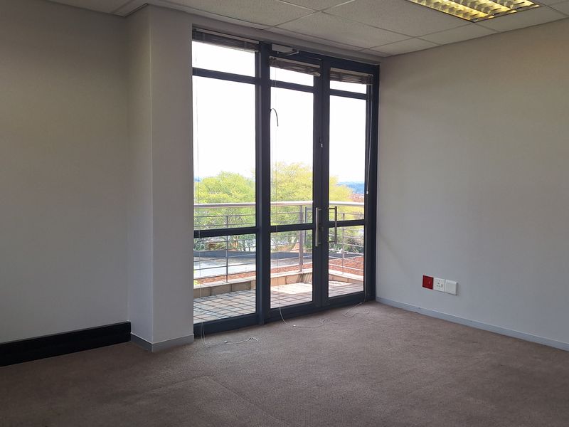A vacant office space featuring neutral carpeting, suspended ceiling tiles with recessed lighting, and direct access to an outdoor balcony through glass doors.