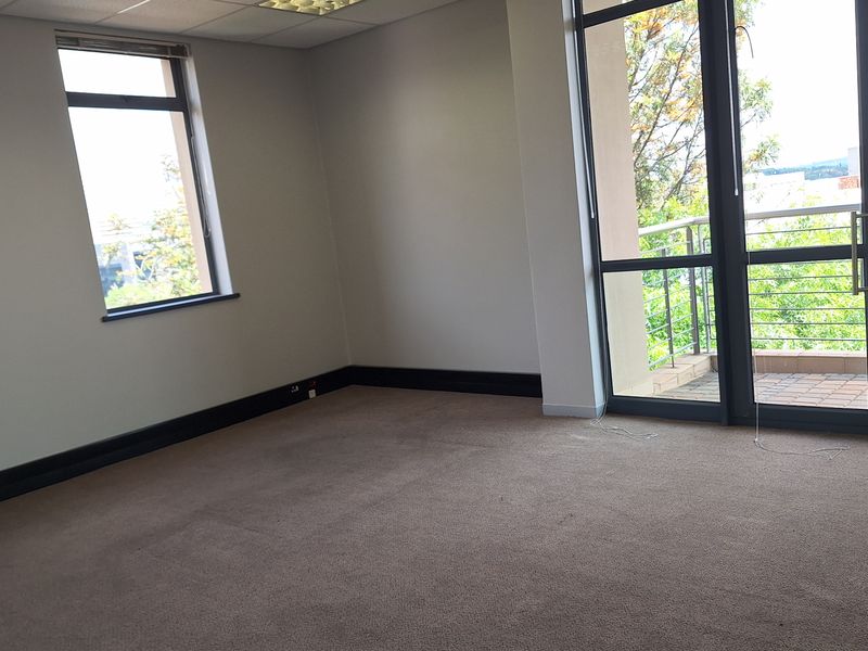A vacant office space featuring a suspended ceiling, recessed lighting, carpeted flooring, and direct access to a private balcony through large aluminium-framed doors.