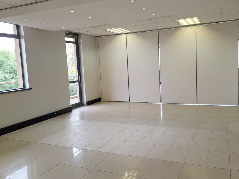 A spacious, empty office area featuring polished tiled flooring, a suspended ceiling with recessed lighting, and a flexible partition wall system.