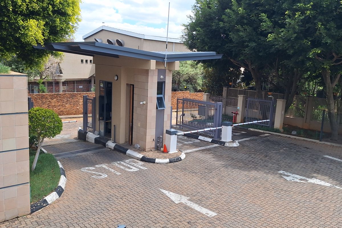 A secure office park entrance featuring a guard house, automated boom gate, and paved driveway with clear traffic markings.