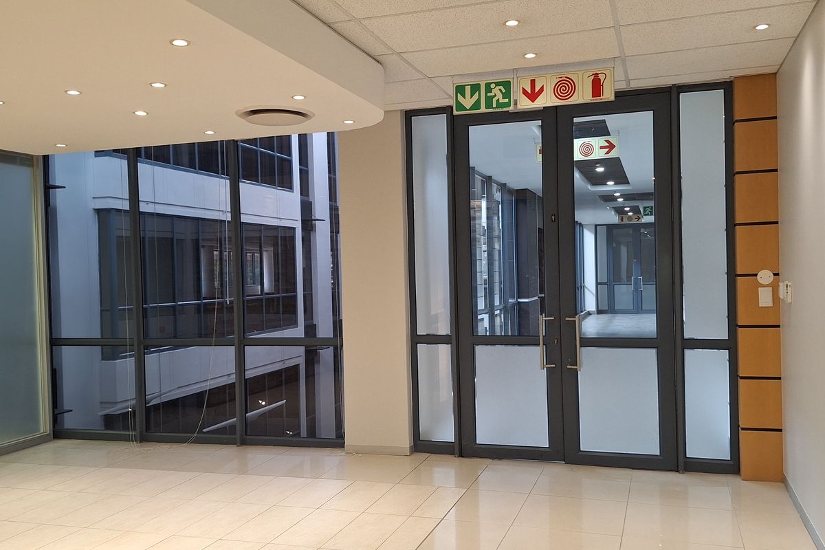 Modern, vacant office space featuring tiled flooring, suspended ceilings with recessed lighting, and glass partitions providing a bright, professional environment.