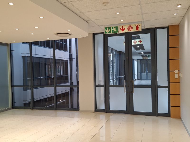Modern, vacant office space featuring tiled flooring, suspended ceilings with recessed lighting, and glass partitions providing a bright, professional environment.