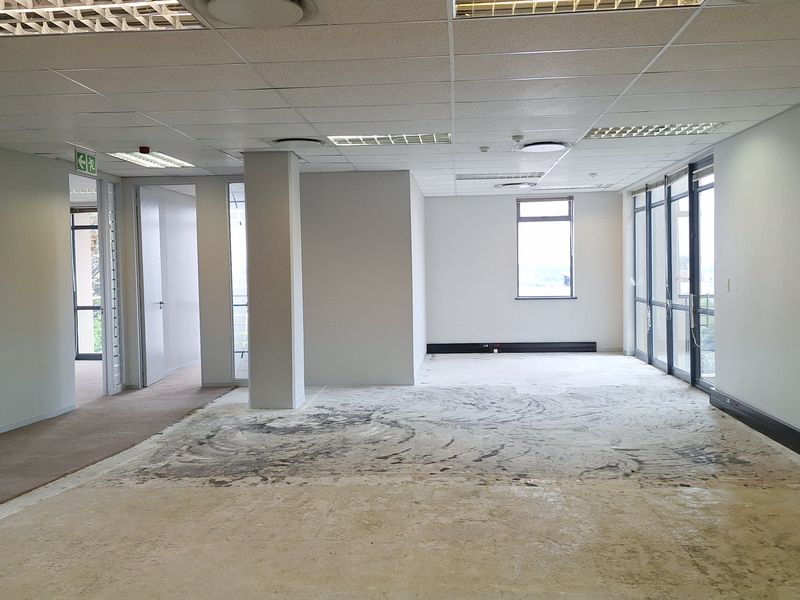 An empty, open-plan office space featuring a suspended ceiling, recessed lighting, and large windows, currently requiring new flooring installation.