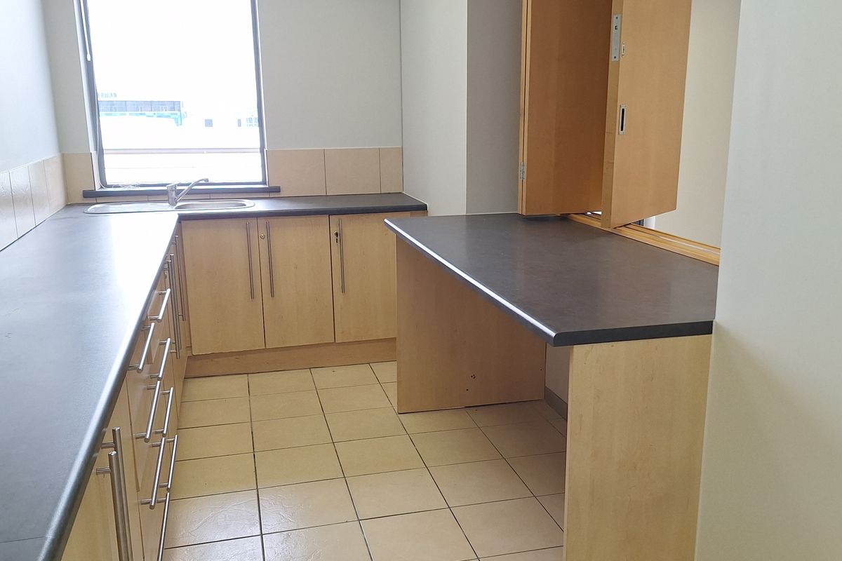 A functional office kitchenette featuring laminate cabinetry, dark countertops, a stainless steel sink, and a convenient bi-fold service window.