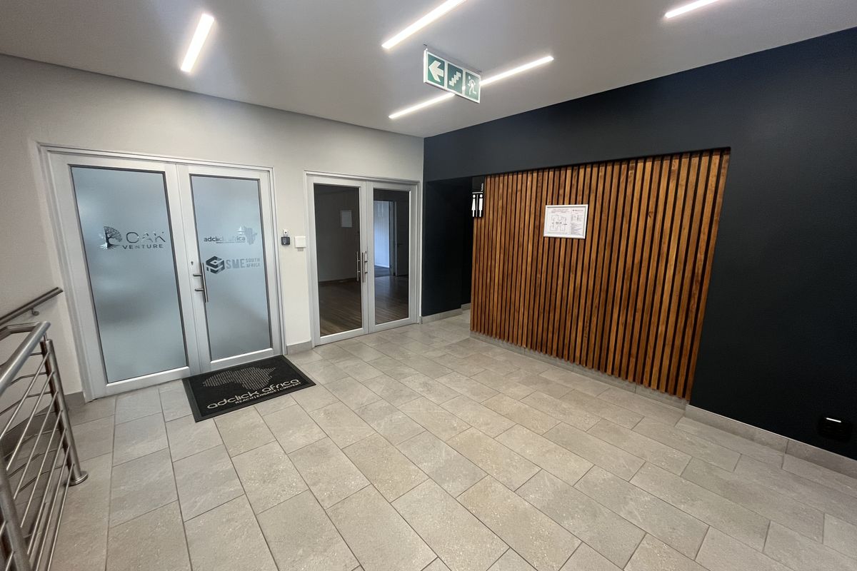 Modern office entrance lobby featuring tiled flooring, a decorative timber slat feature wall, and glass panel doors leading to office suites.