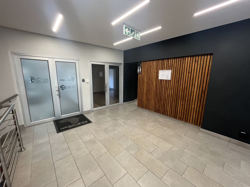 Modern office entrance lobby featuring tiled flooring, a decorative timber slat feature wall, and glass panel doors leading to office suites.